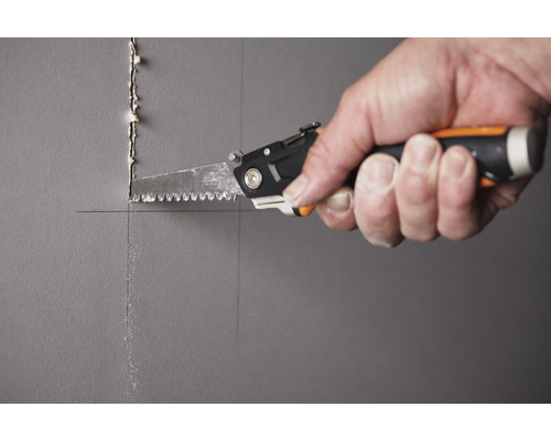 O mână taie o gaură într-un perete cu un fierăstrău de mână.