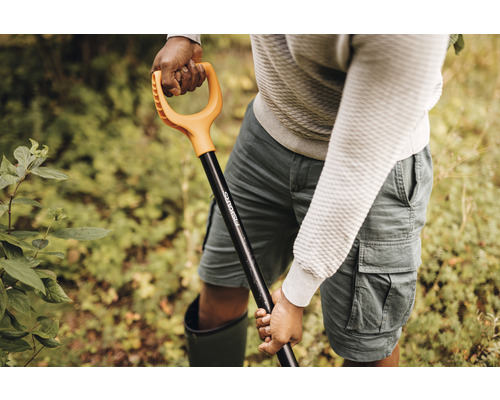 O persoană ține o lopată marca Fiskars în grădină.