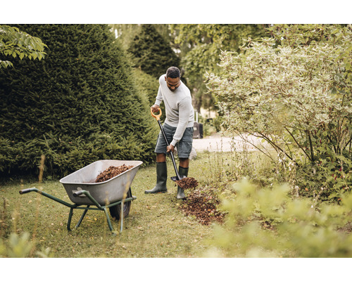 Un bărbat pune frunze într-un cărucior cu o lopată de grădină în grădină.