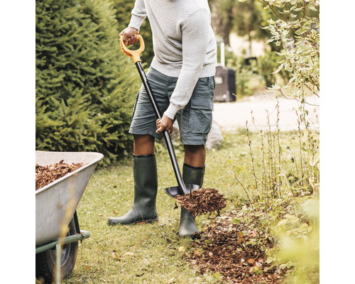 O persoană folosește un hârleț pentru a împrăștia mulci în grădină.
