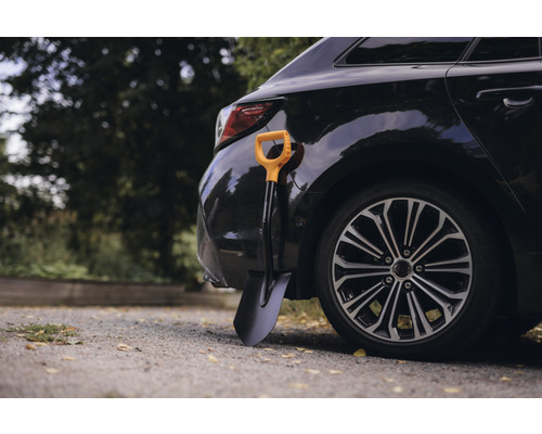 Cazma neagră cu mâner galben sprijinită de o mașină