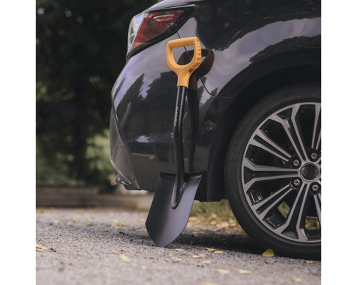 Spată Fiskars sprijinită de o mașină neagră