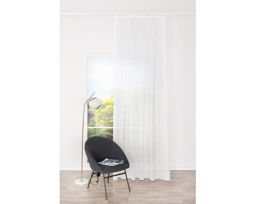 Scenă cu o cortină albă transparentă în fața unei ferestre, un scaun gri și o lampă de podea