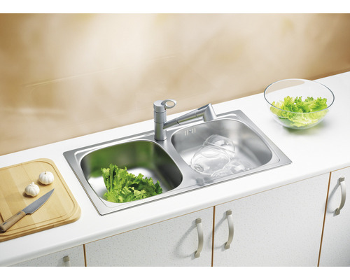 Chiuvetă din oțel inoxidabil cu uscător, robinet, salată, vase, tocător și usturoi pe un blat de bucătărie