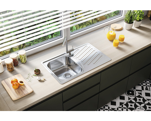 Scenă de bucătărie cu chiuvetă, baterie și blat de lucru în fața unei ferestre.