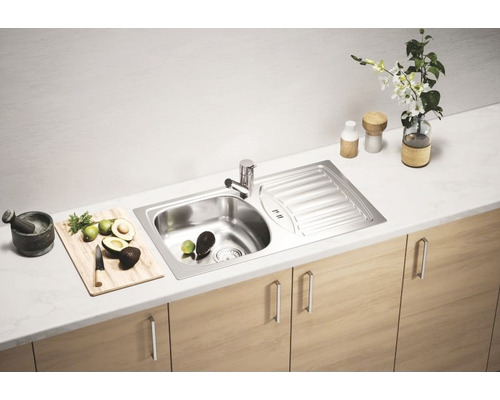 Scenă de bucătărie cu chiuvetă, robinet și ingrediente proaspete pe un blat de lucru deasupra dulapurilor de bază.