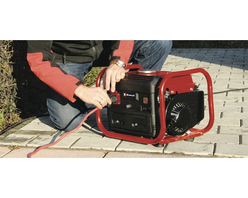 Un bărbat conectează un cablu de alimentare roșu la un generator marca Einhell.