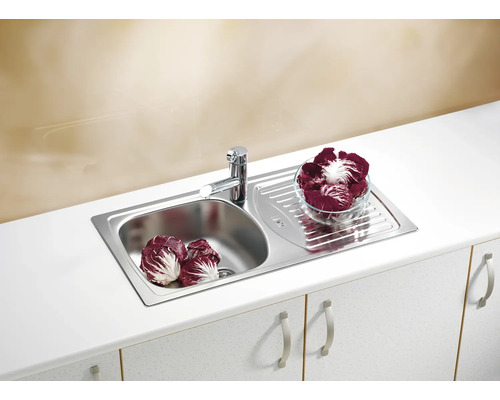 Chiuvetă din oțel inoxidabil cu uscător și robinet pe un dulap de bucătărie alb cu legume