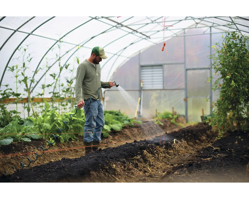 Bărbat udând plante într-o seră cu un furtun de grădină