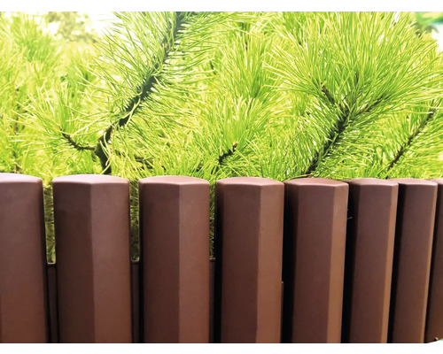 Gard din plastic cu aspect de lemn și ramuri verzi de conifere în fundal.