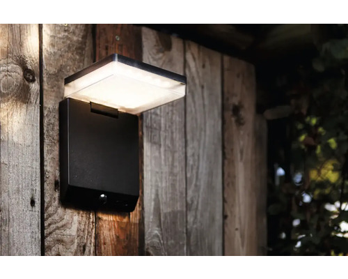 Lumină de perete LED neagră pentru exterior cu senzor de mișcare pe un perete de lemn