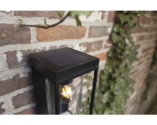 Lampă solară cu abajur transparent pe perete de cărămidă