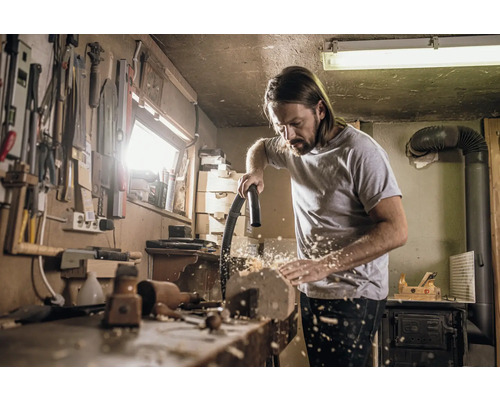Bărbat curăță bancul de lucru cu aspiratorul în atelier