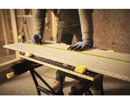 Artizan măsoară o scândură de lemn pe un banc de lucru cu o ruletă.