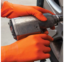 Mâini cu mănuși de protecție care operează o cheie de impact pe o roată.