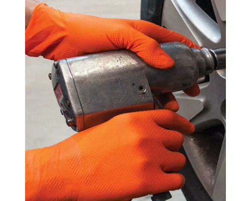 Mâini cu mănuși de protecție care operează o cheie de impact pe o roată.