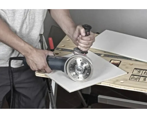 Bărbat taie o faianță cu un polizor unghiular pe un banc de lucru