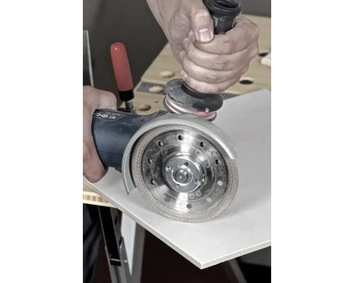 Prim-plan cu o persoană care lucrează o țiglă cu un polizor unghiular.