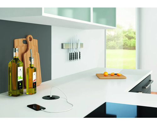 Scenă de bucătărie cu sticle de ulei de măsline, tocătoare, suport magnetic pentru cuțite și smartphone cu încărcător pe un blat alb.