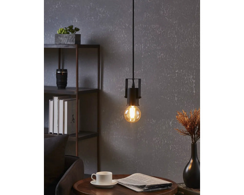 Fotografie de interior cu o lampă suspendată cu bec deasupra unei mese cu ziar și ceașcă.