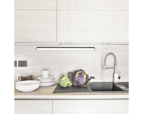 Bucătărie luminoasă cu chiuvetă, robinet, veselă, legume și iluminat sub dulap