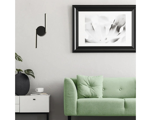 Cameră de zi cu o lampă de perete neagră, o canapea verde și o imagine înrămată