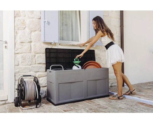 Femeie aranjând unelte de grădinărit într-o cutie de depozitare gri în aer liber