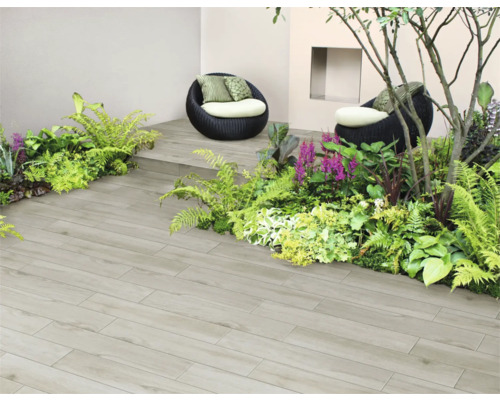 Zonă de grădină cu plăci de terasă cu aspect de lemn, plantată cu ferigi și plante ornamentale, precum și două fotolii.