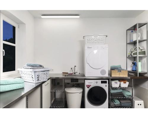 O spălătorie luminoasă cu mașină de spălat, uscător, rafturi și coșuri de rufe.