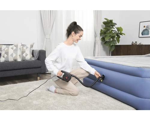 Femeie umflând o saltea pneumatică cu o pompă electrică într-un living luminos