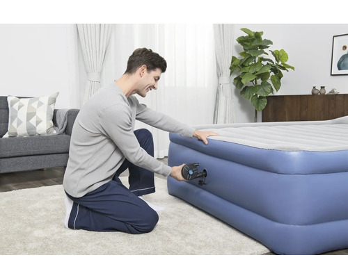 Un bărbat umflă o saltea gonflabilă cu o pompă