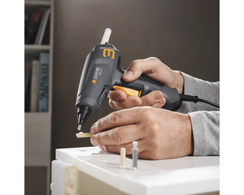 O persoană folosește pistolul de lipit cu topire Steinel pentru a lipi bucăți de lemn pe o suprafață albă