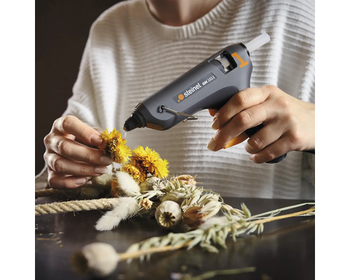 Utilizator care fixează flori pe o coroană cu un pistol de lipit