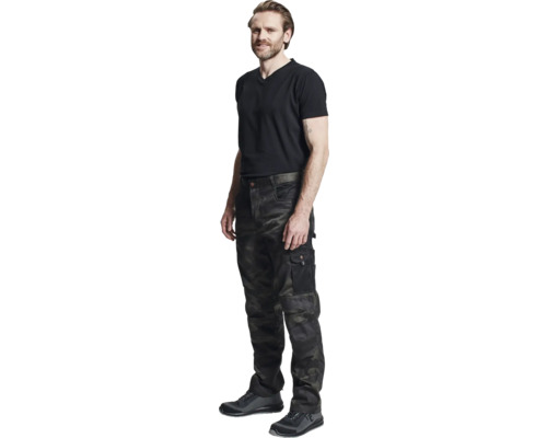 Bărbat în haine de lucru cu pantaloni de camuflaj, tricou și pantofi de protecție.