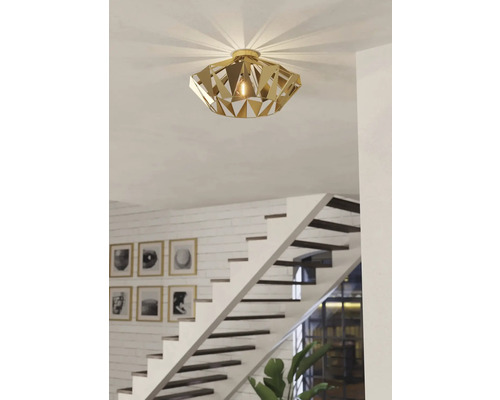 Plafonieră aurie cu design geometric într-un spațiu de locuit cu scară.