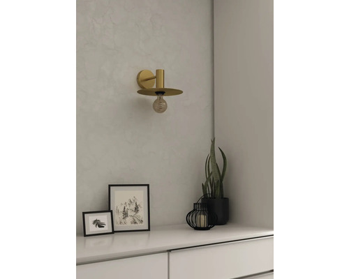 Lampa de perete de culoare aurie deasupra unei comode albe cu decorațiuni