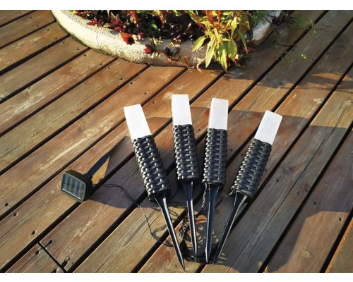 Patru lămpi solare cu țăruș de pământ pe o terasă de lemn.