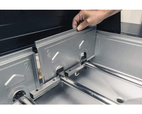 O persoană introduce un apărător de flacără din oțel inoxidabil într-un grătar cu gaz.