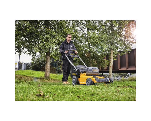 Un bărbat manevrează o mașină de tuns iarba DeWalt în grădină.