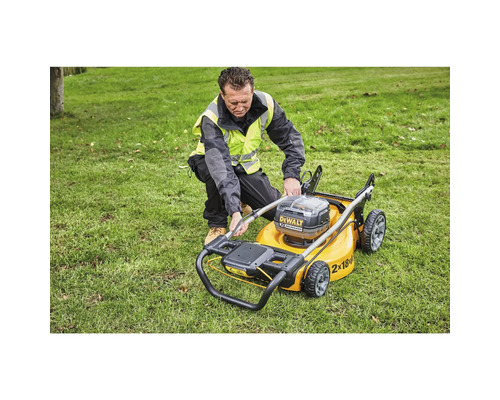 Un bărbat manevrează o mașină de tuns iarba galbenă, cu acumulator, pe un gazon.
