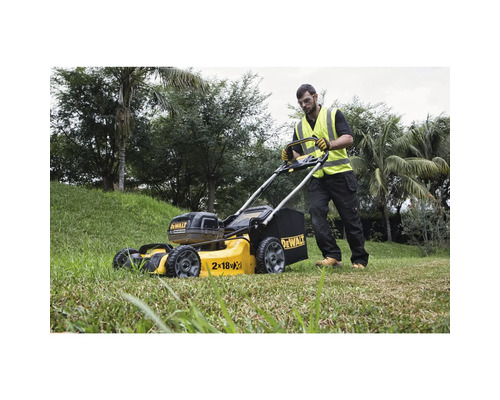 Un bărbat operează o mașină de tuns iarba galbenă, cu acumulator, marca DeWalt, în grădină.