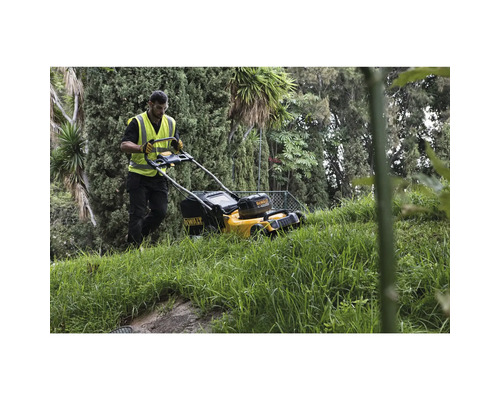 O persoană operează o mașină de tuns iarba DeWalt într-o grădină cu copaci.