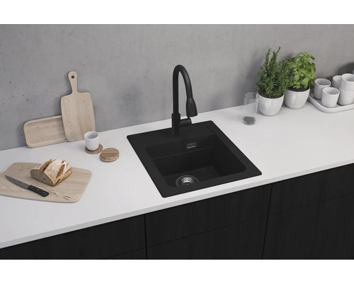 Chiuvetă de bucătărie neagră cu baterie pe un blat de bucătărie cu alimente și plante