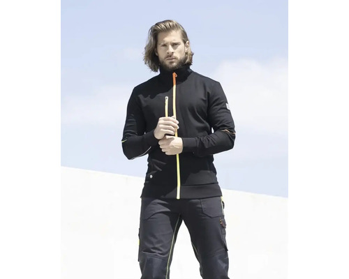 Bărbat poartă o jachetă de lucru și pantaloni de lucru negri.