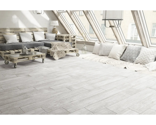 Cameră luminoasă cu gresie aspect lemn, mobilier din paleți și ferestre de mansardă.