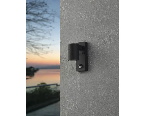 Lumină de perete exterioară neagră cu senzor de mișcare montată pe un perete.