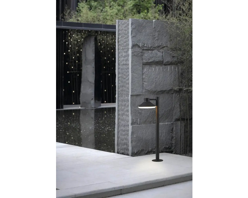 Scenă exterioară cu o potecă de grădină și corp de iluminat de grădină în fața unui zid de piatră.