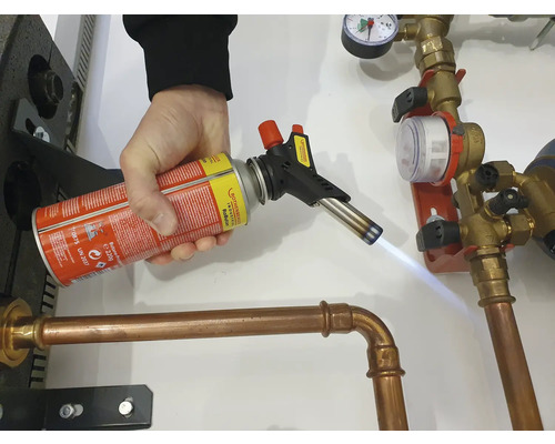 O persoană sudează o țeavă de cupru cu un arzător cu gaz.