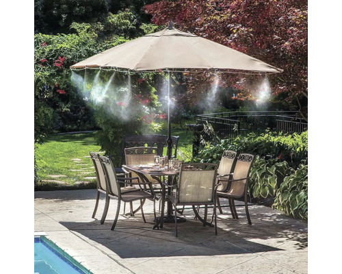 Scenă de grădină cu masă de sufragerie, scaune, umbrelă de soare și duze de pulverizare pentru răcire