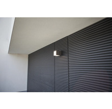 Lumină de perete pătrată pe o fațadă cu structură liniară orizontală.